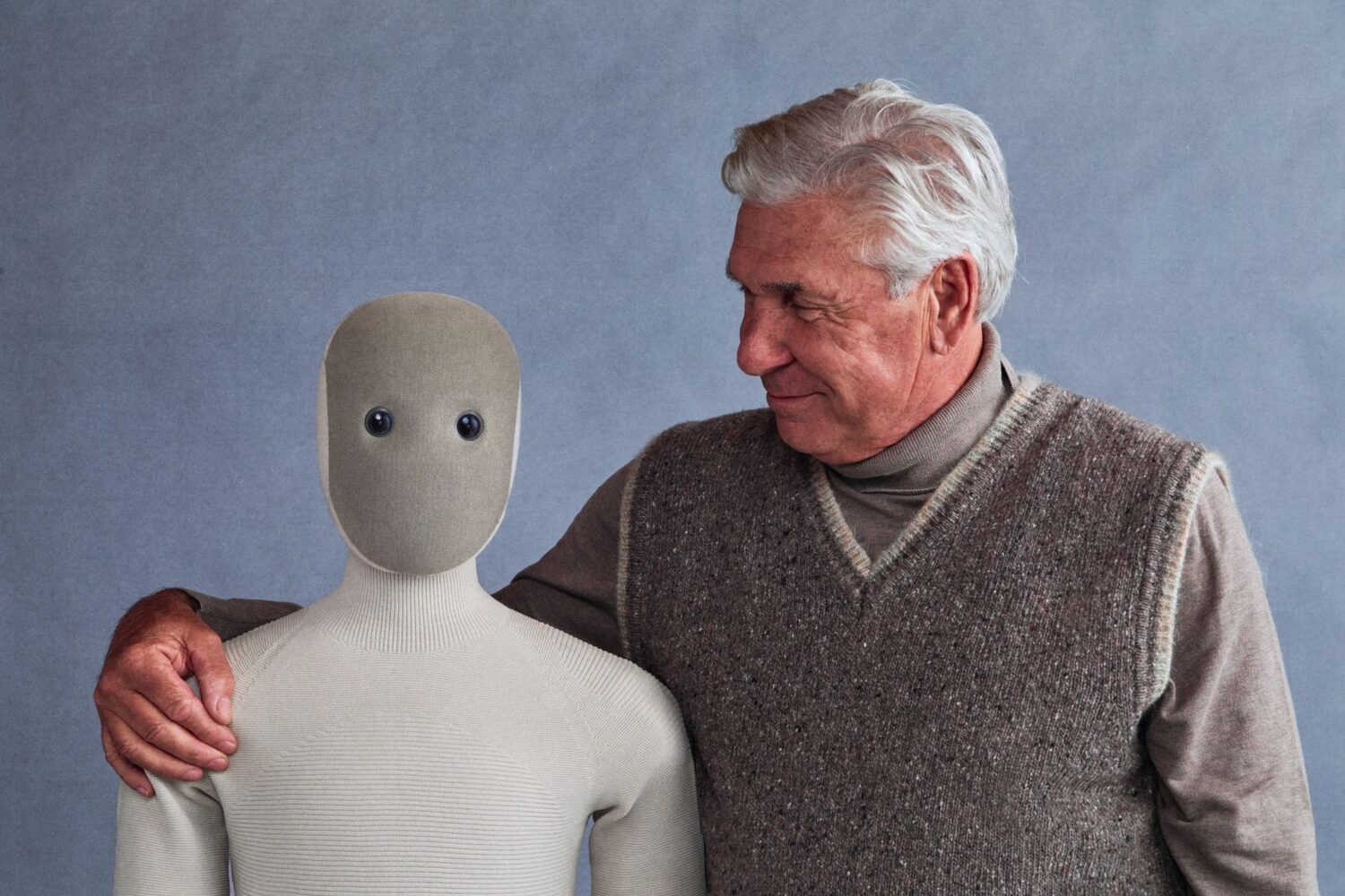 The 1X NEO home robot, in a knitted cover, standing beside an older man